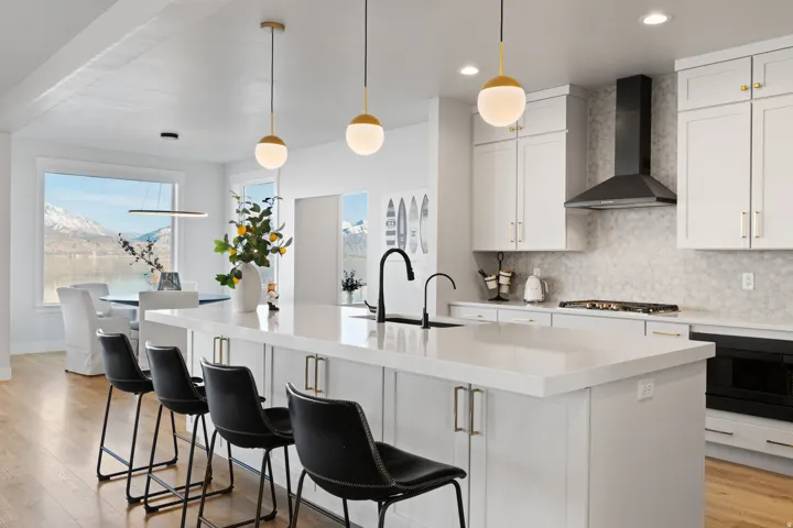 Spacious kitchen featuring a large central island with seating, white shaker-style cabinetry, a built-in cooktop with a black range hood, and light-toned backsplash tiling