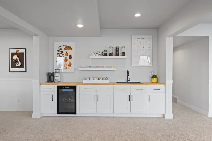 Integrated wet bar with white cabinetry, wood-finish countertop, and black sink with matte black faucet