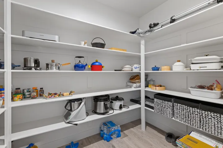 Spacious walk-in pantry featuring extensive white shelving, wood-finish flooring, and ample storage capacity