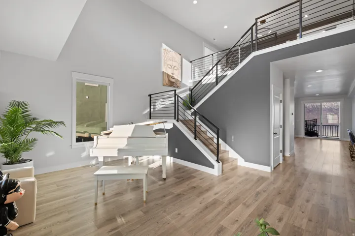 Two-story interior featuring a modern staircase with dark metal railings, light wood-finish flooring throughout, high vaulted ceilings, and a second-story loft area