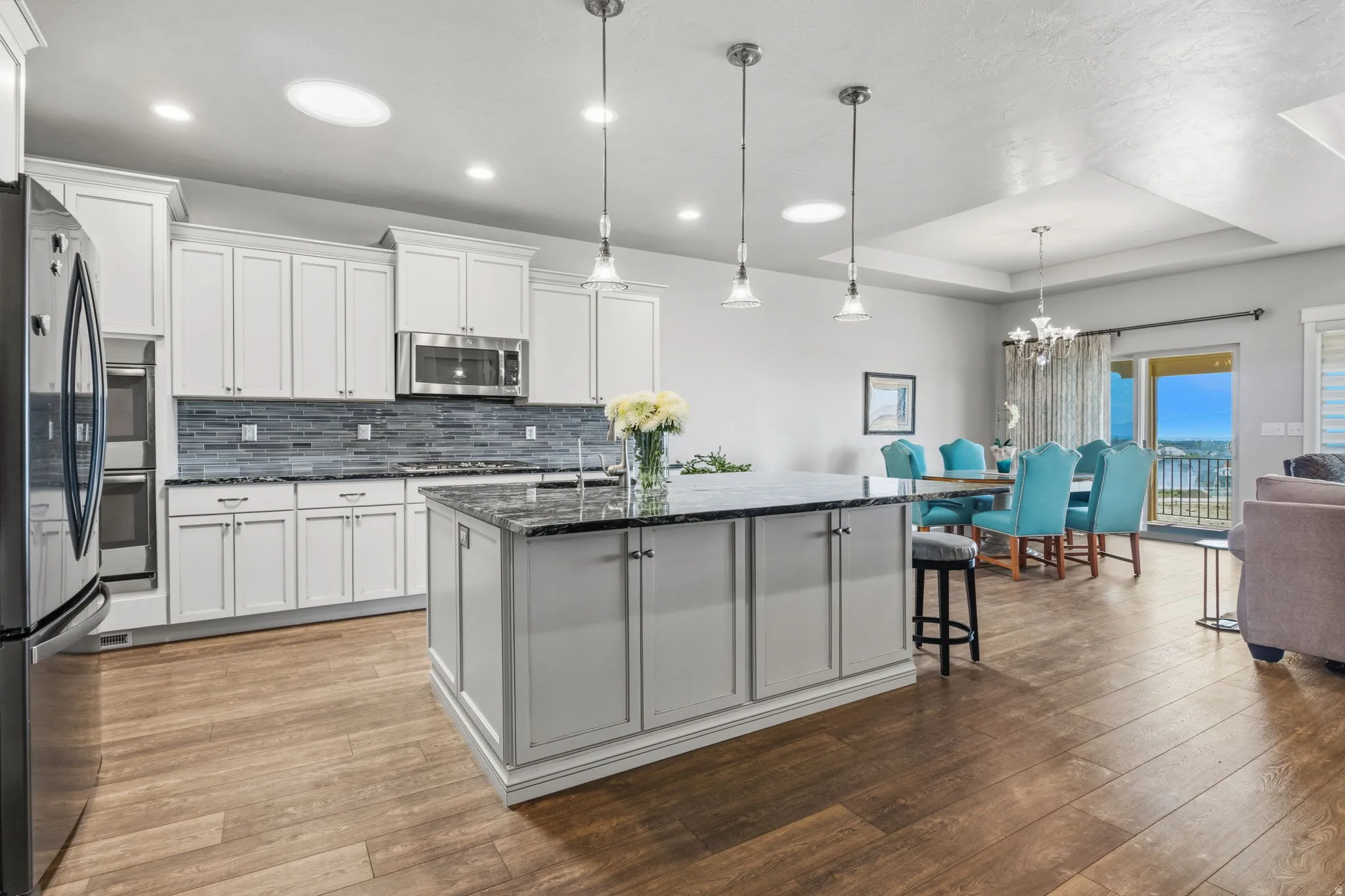 Open-concept kitchen and dining area featuring wood-finish flooring, white cabinetry, dark stone countertops, and a full suite of stainless steel appliances.  The island has full storage access on the front and back.
