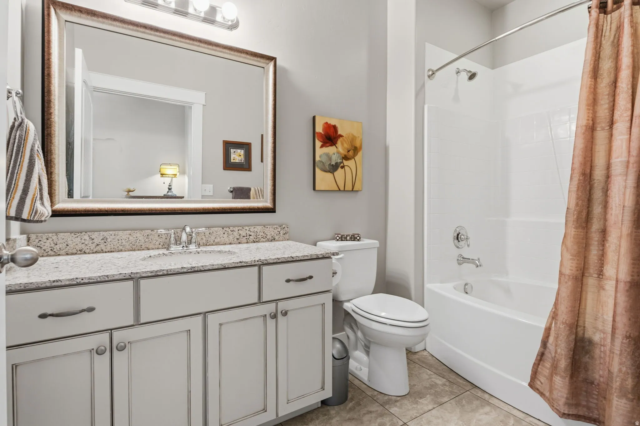 Guest Bathroom featuring a single vanity with Granite countertop, white cabinetry with dark hardware, a rectangular framed mirror with overhead lighting, a white toilet, and a  high white tub/shower combination