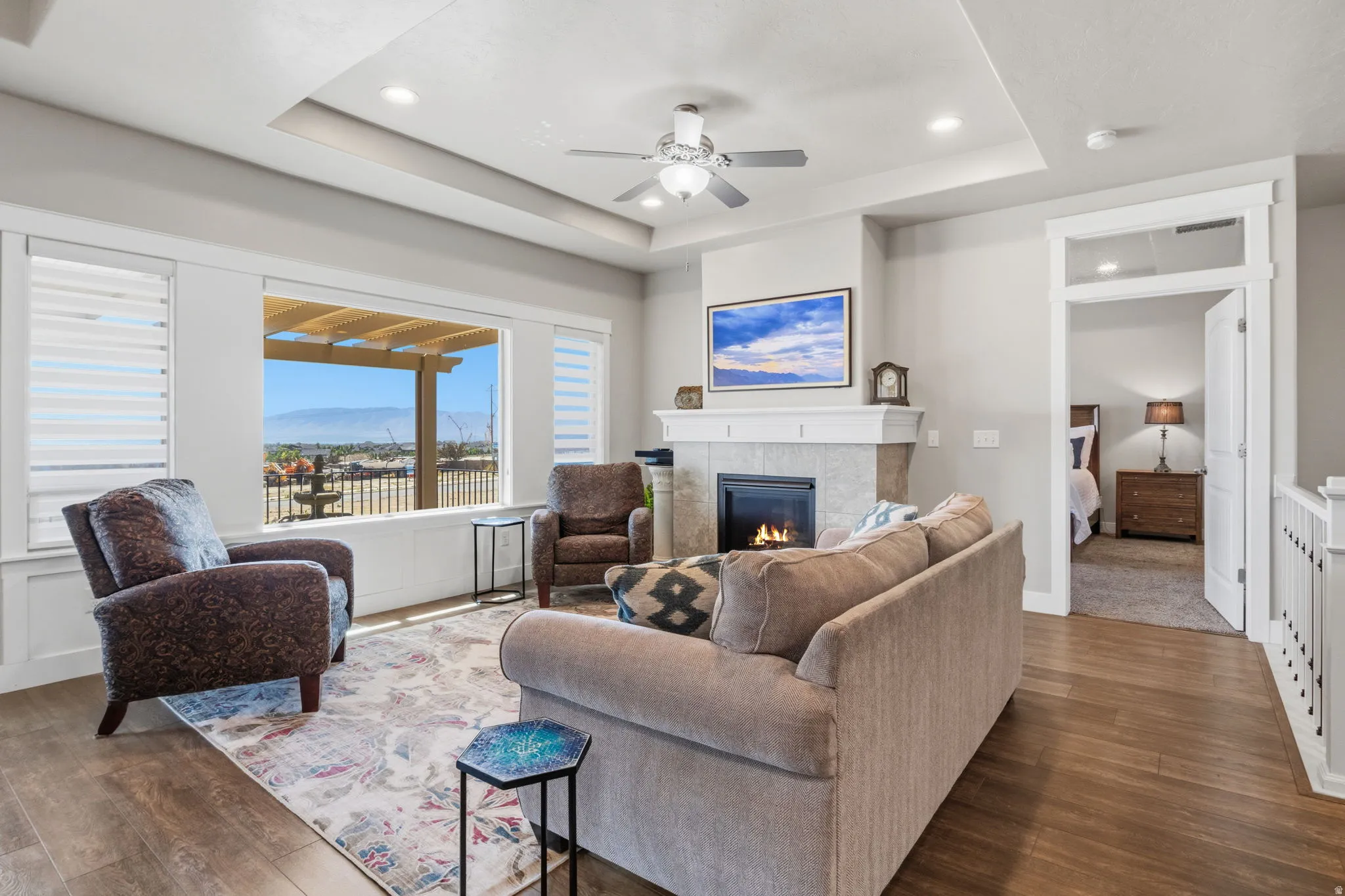Living area featuring a gas fireplace with a stone surround, wood-finish flooring, a tray ceiling with recessed lighting, and a window overlooking the valley.