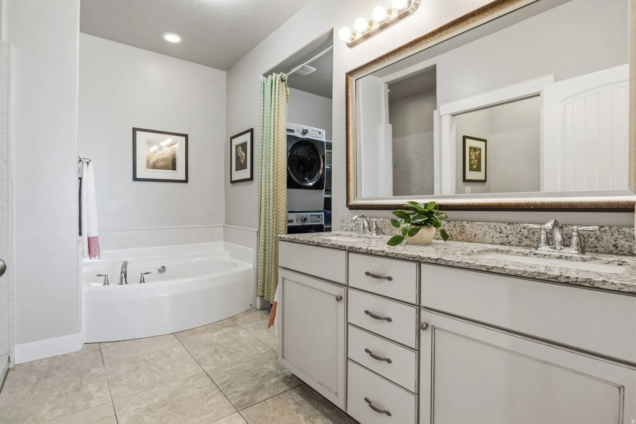 Spa-inspired primary bathroom featuring a GREAT soaking tub, a dual-sink vanity with a granite countertop, a large framed mirror with integrated lighting, and ceramic tile flooring.  Check out all that storage.