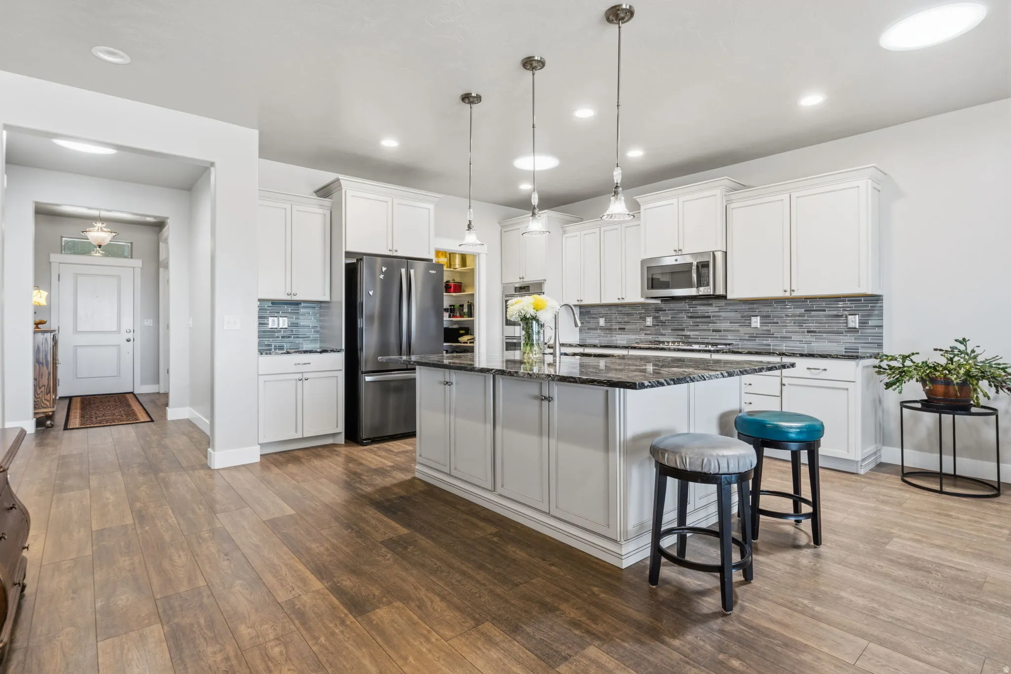 Kitchen featuring a central island, white cabinetry, integrated stainless steel appliances, a tile backsplash, and wood-finish flooring