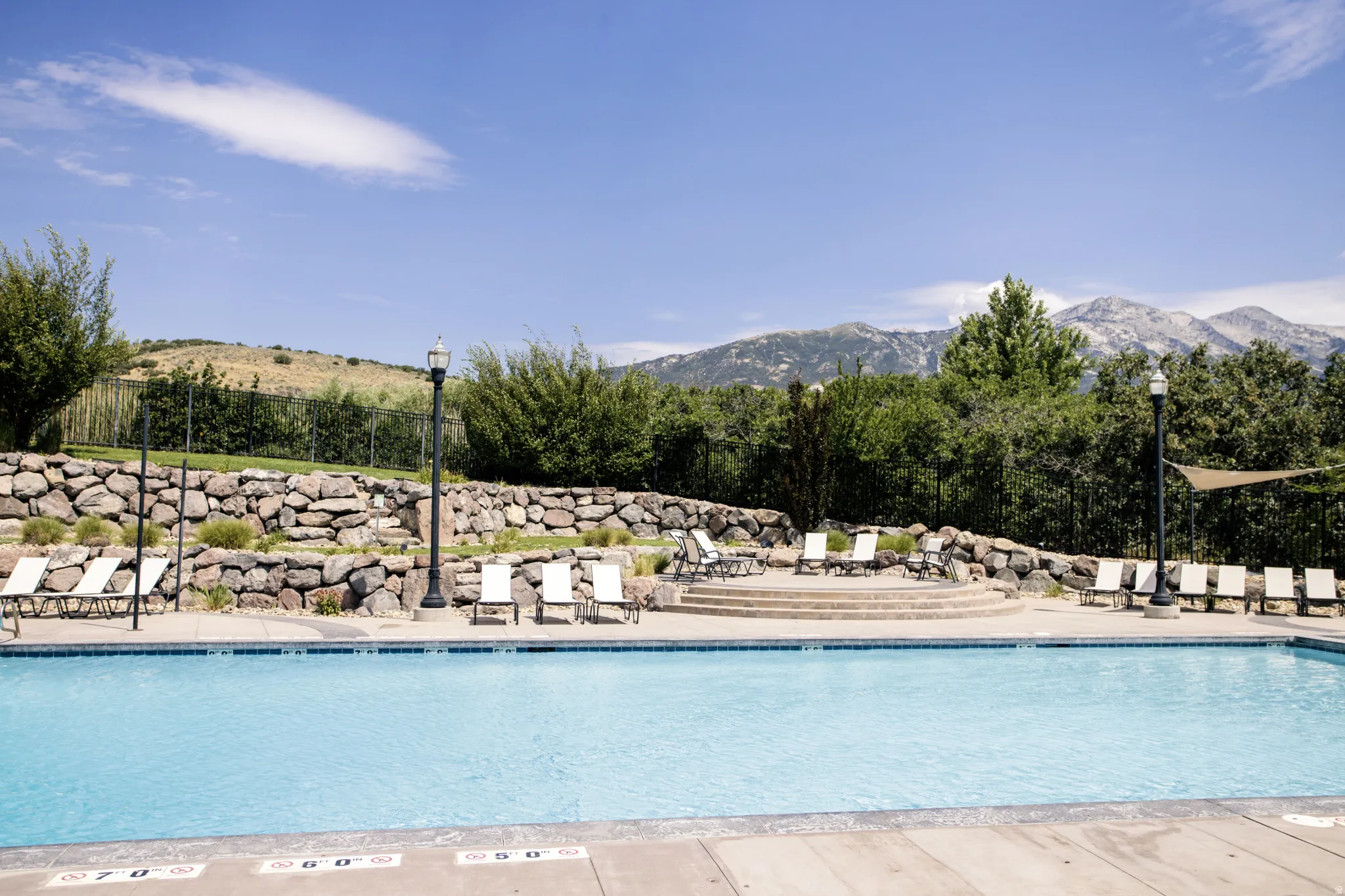 Outdoor HEATED swimming pool with integrated sun ledge and concrete decking, surrounded by lounge chairs