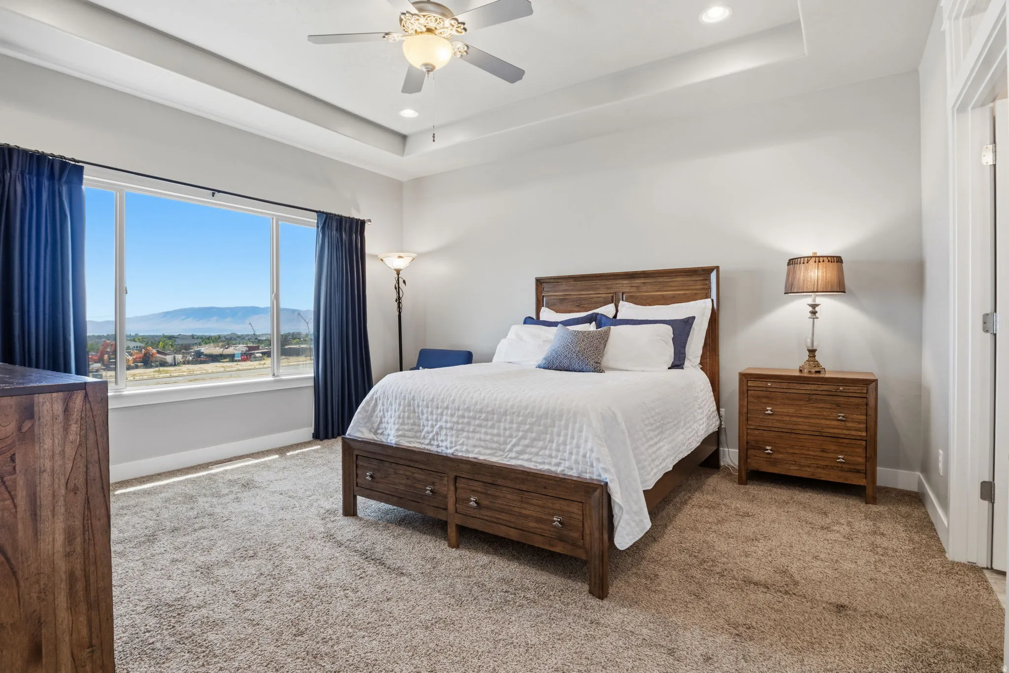 Primary bedroom with comfy carpet. This suite features a large picture window with mountain scenery, a tray ceiling, recessed lighting, plenty of space for your accessories, and a ceiling fan.  Be sure to check out the VIEW!!!