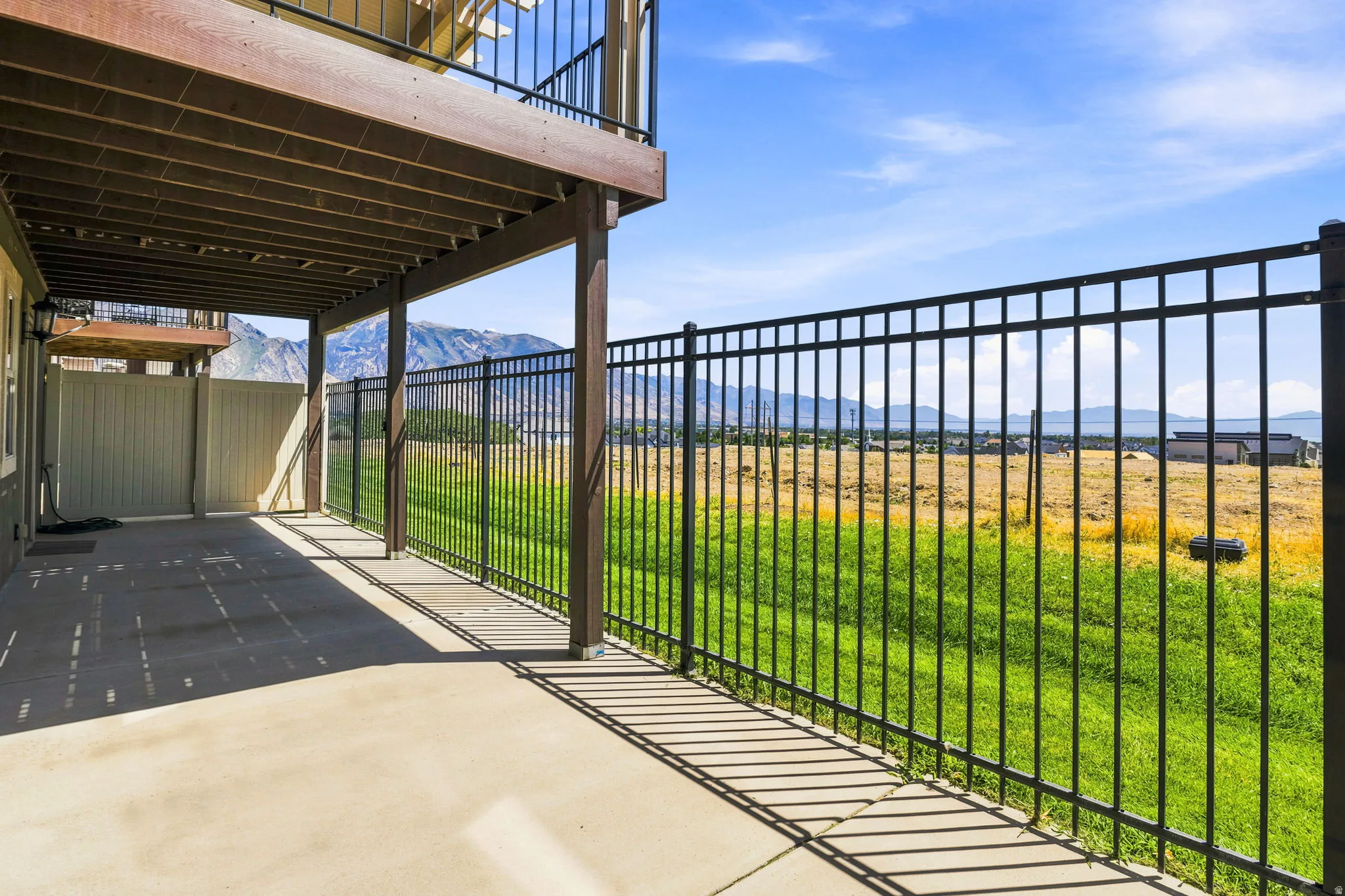 Covered patio with concrete flooring, supported by structural columns, featuring an overhead deck with black metal railings. Gate key available.