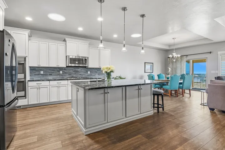 Open-concept kitchen and dining area featuring wood-finish flooring, white cabinetry, dark stone countertops, and a full suite of stainless steel appliances.  The island has full storage access on the front and back.
