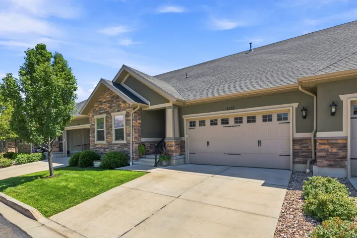 Modern townhouse exterior featuring stone veneer accents, an attached two-car garage with decorative hardware, a covered entry, and a manicured lawn