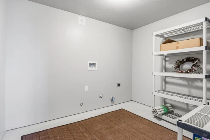 Dedicated utility area located right at the bottom of the stairs.  Featuring washer and dryer hookups, light gray wall paint, overhead lighting, and room for lots of storage shelves.