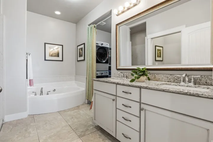 Spa-inspired primary bathroom featuring a GREAT soaking tub, a dual-sink vanity with a granite countertop, a large framed mirror with integrated lighting, and ceramic tile flooring.  Check out all that storage.