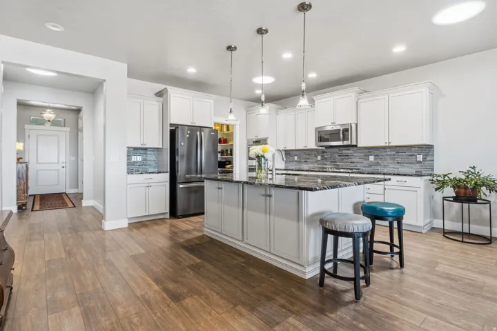 Kitchen featuring a central island, white cabinetry, integrated stainless steel appliances, a tile backsplash, and wood-finish flooring