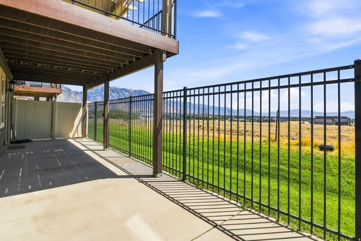 Covered patio with concrete flooring, supported by structural columns, featuring an overhead deck with black metal railings. Gate key available.