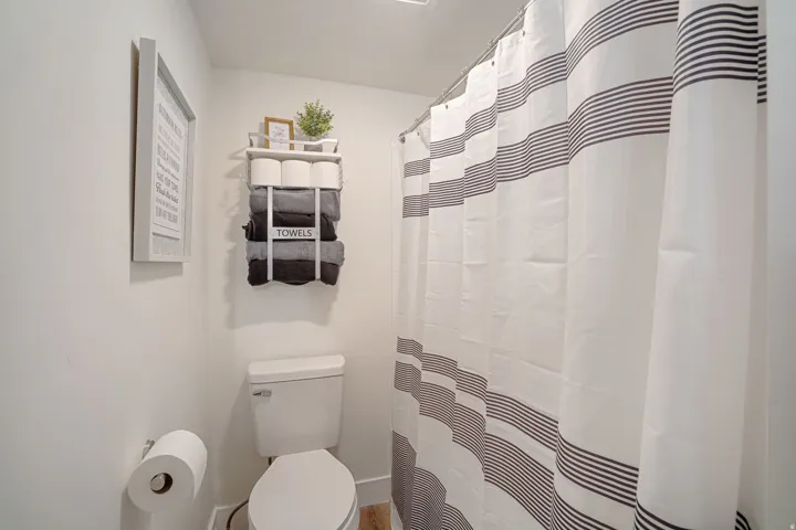 Bathroom featuring a white toilet, white walls, and a shower with a striped curtain