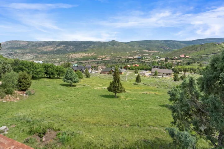 Expansive green landscape with distant residential properties, framed by distant mountains under a blue sky with scattered clouds