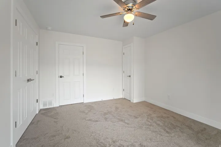 Neutral carpeted room featuring white walls, three paneled doors with brushed nickel hardware, and a ceiling fan with integrated lighting