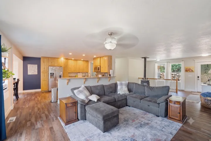 Open-concept living space featuring wood-finish flooring, a kitchen with natural wood cabinetry and stainless steel appliances, a breakfast bar, and a visible wood-burning stove