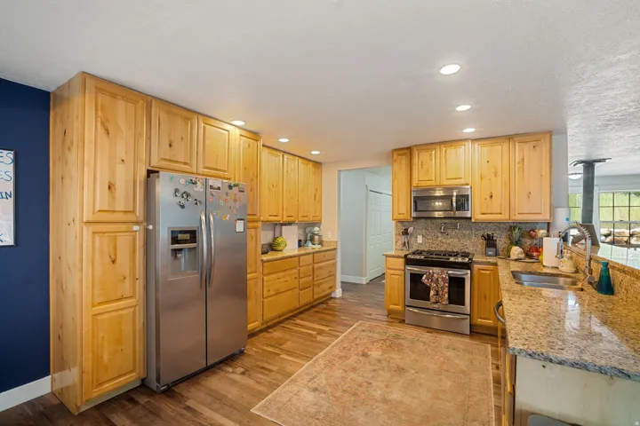 Kitchen featuring extensive natural wood cabinetry, stainless steel appliances, granite countertops, and wood-finish flooring