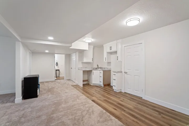 Open-concept room featuring wood-finish flooring, white cabinetry with silver hardware, a stainless steel sink, and light-toned countertops