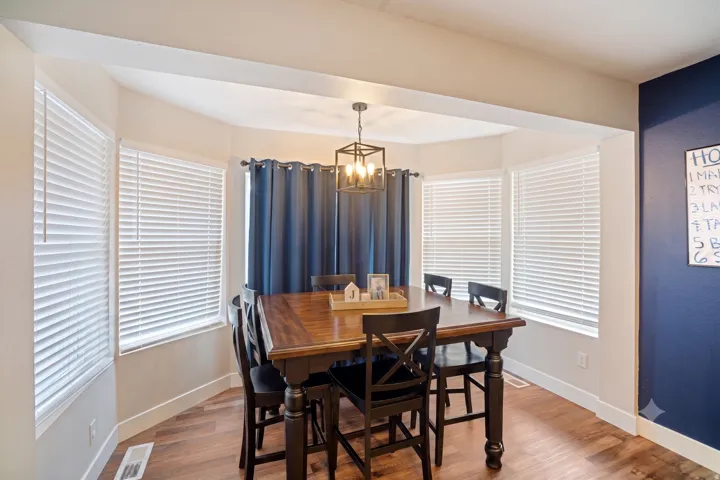 Dining area featuring bay windows, wood-finish flooring, a contemporary chandelier, and a contrasting accent wall