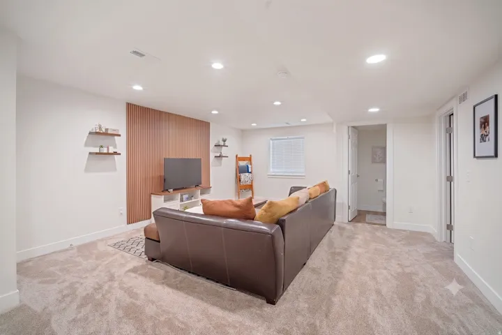 Spacious living area featuring neutral carpet flooring, recessed lighting, and a contemporary accent wall with vertical wood paneling