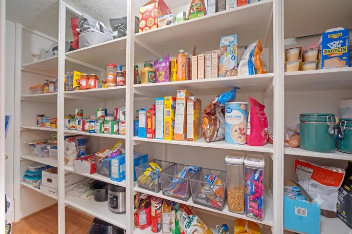 Spacious pantry featuring multiple white shelving units and wood-finish flooring