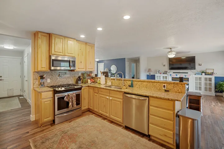 Kitchen featuring natural wood cabinetry, stainless steel appliances, speckled stone countertops, and a coordinating stone backsplash