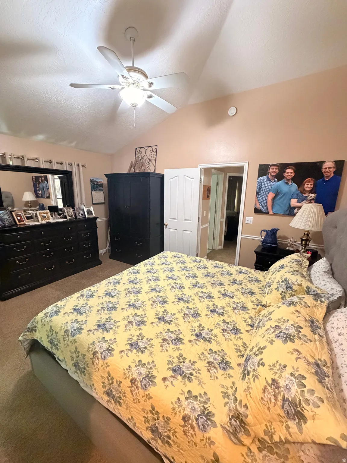 Vaulted ceiling with a ceiling fan, carpet flooring, a white paneled door, and neutral-toned walls
