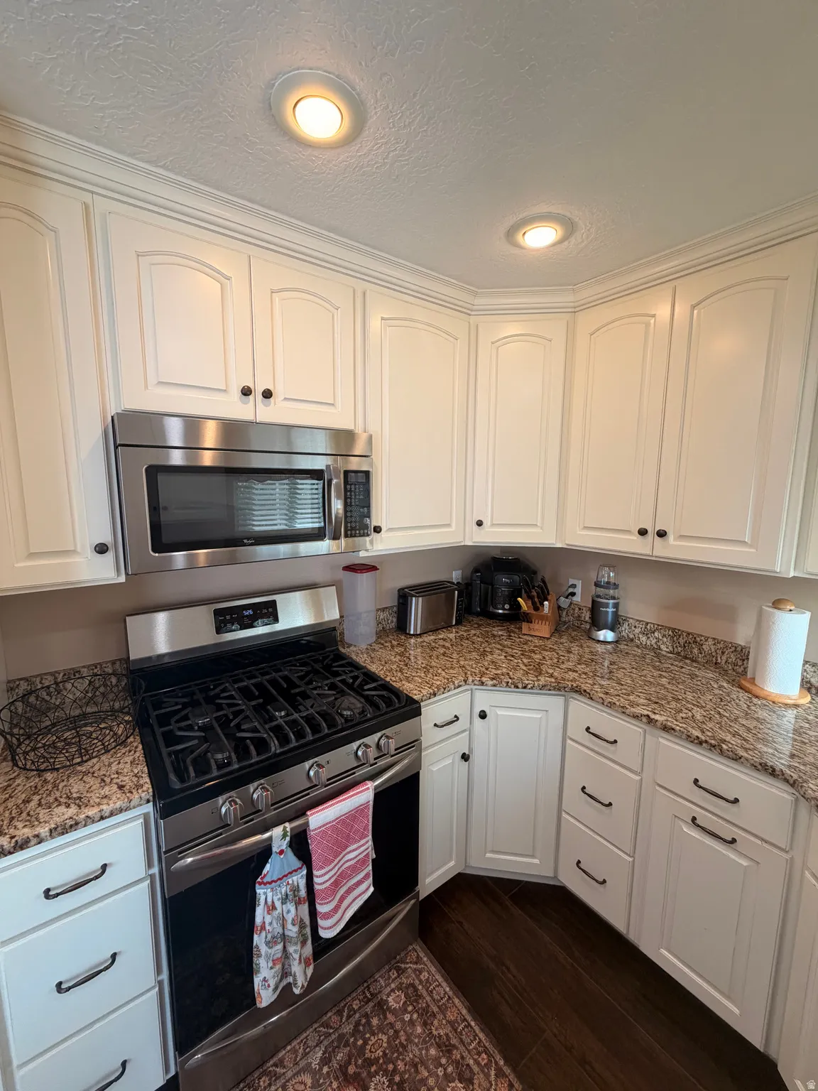 Kitchen featuring white cabinetry with dark hardware, stainless steel gas range, built-in stainless steel microwave, granite-look countertops, and recessed lighting