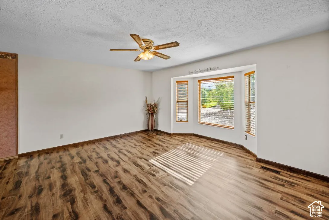 Wood-finish flooring throughout, bay windows with natural wood blinds, ceiling fan with integrated lighting, and neutral wall tones