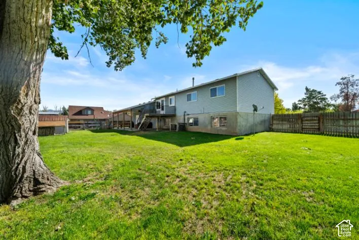 Expansive lawn area, mature tree, multi-level deck, fenced perimeter, and wood siding on the upper level