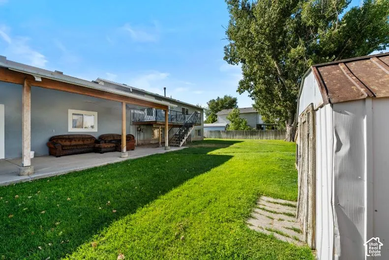 Expansive backyard featuring a manicured lawn, mature shade trees, and a covered patio area with concrete flooring