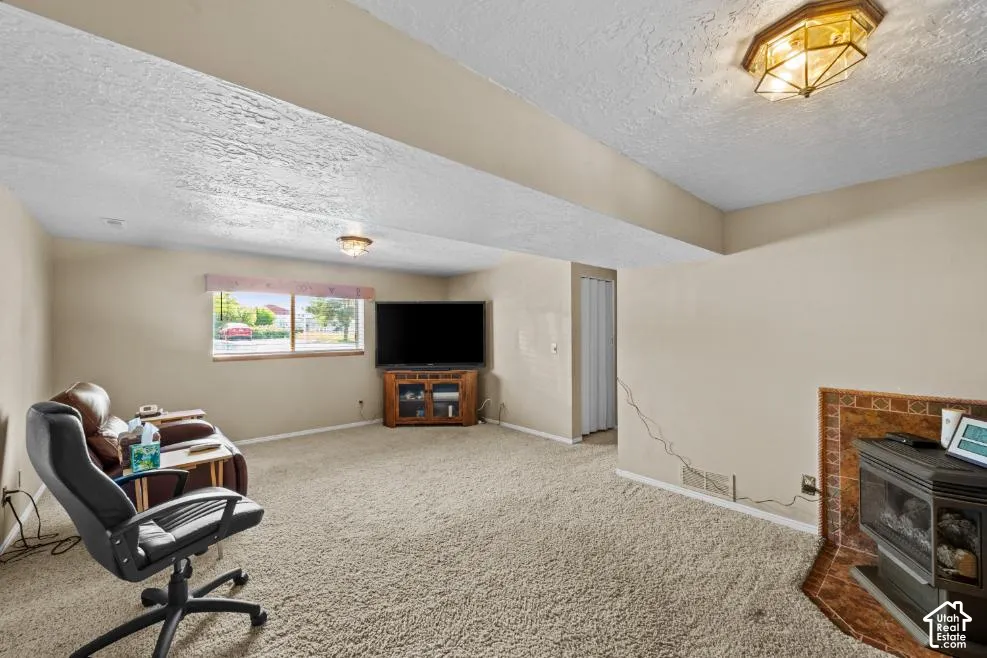 Carpeted living space featuring a window, built-in light fixtures, and a corner fireplace with a tiled surround