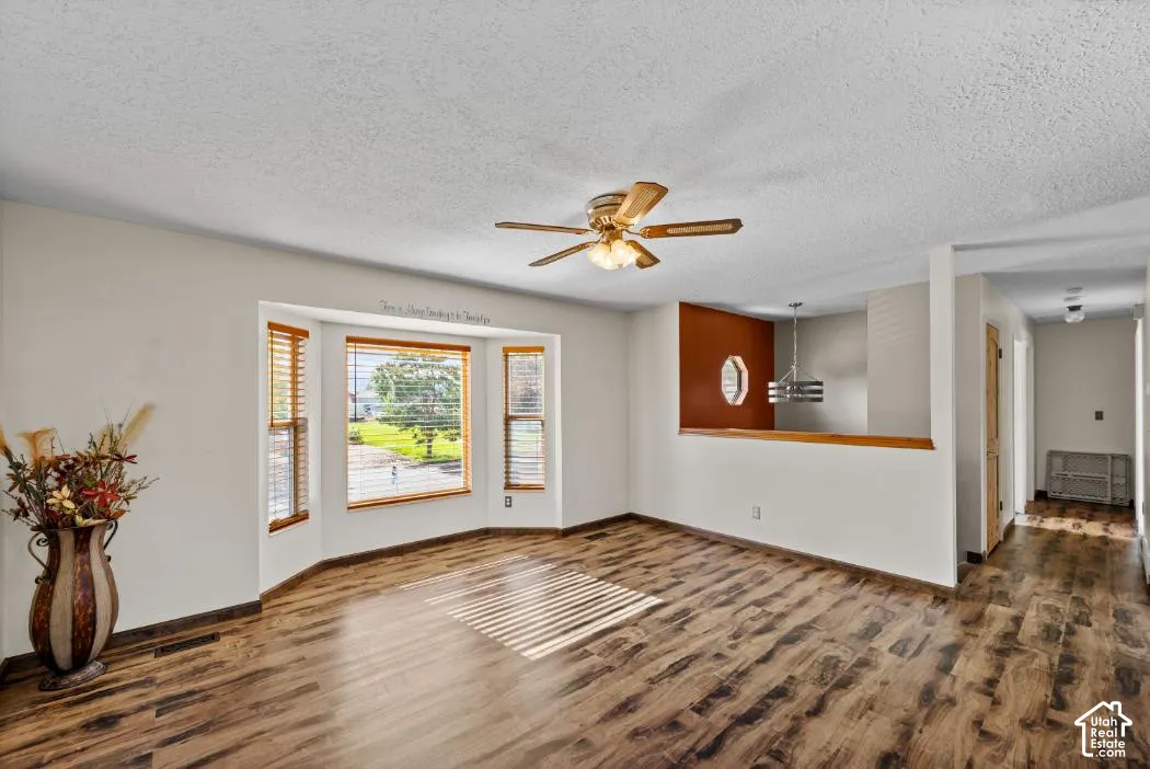 Wood-finish flooring, bay window with wood blinds, ceiling fan, and a partial wall with a decorative cutout