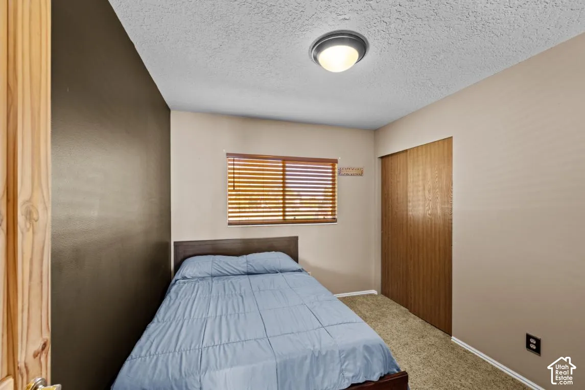 Compact bedroom featuring a wood-finish door, horizontal wood-slat window with natural light, textured ceiling with recessed lighting, and neutral wall finishes