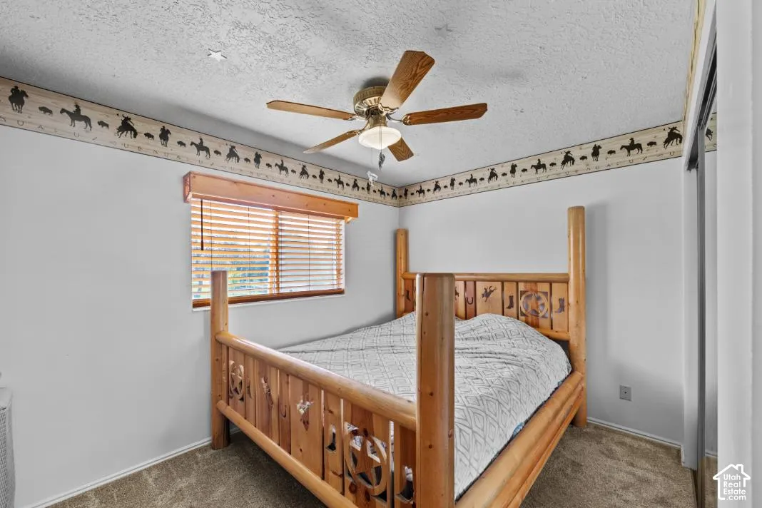 Master bedroom featuring a custom wooden four-poster bed with carved detailing, ceiling fan with wood blades, wood-framed window with horizontal blinds, and decorative border trim along the ceiling line