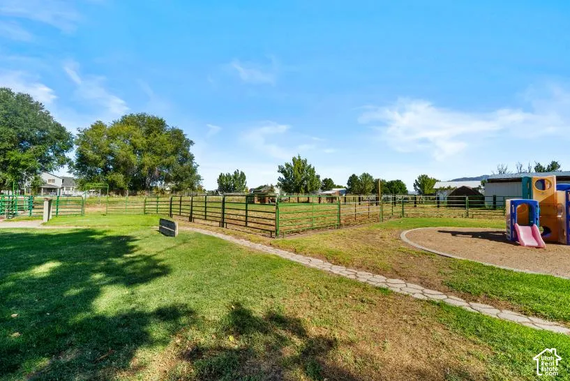 Expansive rural property featuring mature shade trees, white fencing, manicured lawn, recreational playground equipment, and outbuildings with metal roofing visible in the distance