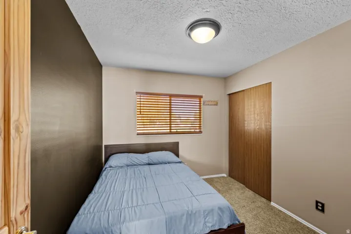 Compact bedroom featuring a wood-finish door, horizontal wood-slat window with natural light, textured ceiling with recessed lighting, and neutral wall finishes
