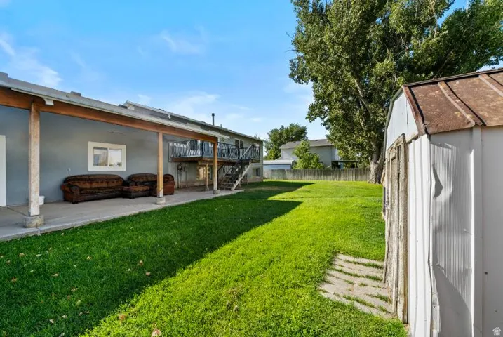 Expansive backyard featuring a manicured lawn, mature shade trees, and a covered patio area with concrete flooring