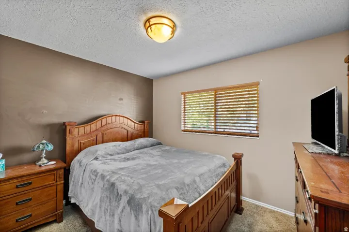 Comfortable secondary bedroom showcasing warm wood-finish furnishings, neutral wall tones, and natural light from shuttered windows