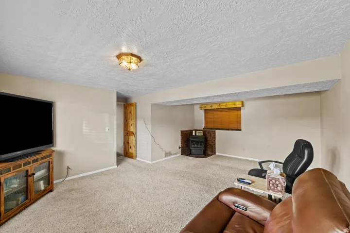 Spacious basement recreation room featuring neutral carpet flooring, textured ceiling, recessed lighting, and built-in wood cabinetry with glass-front display shelving
