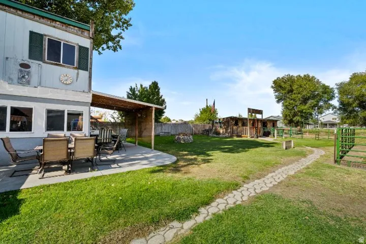 Expansive backyard featuring a concrete patio with a covered pergola, a stone-lined pathway, and mature trees