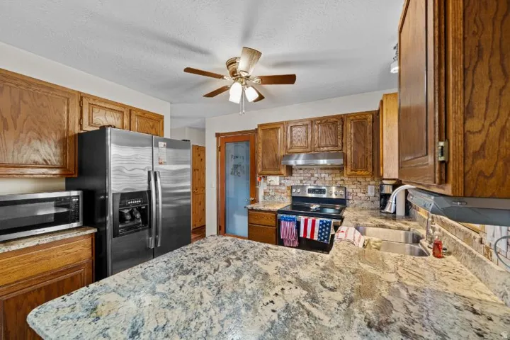 Kitchen featuring wood cabinetry, stainless steel appliances, a ceiling fan, and stone countertops