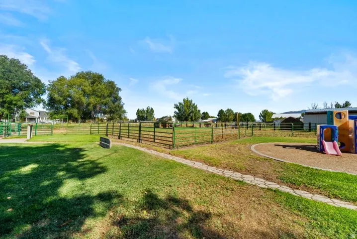 Expansive rural property featuring mature shade trees, white fencing, manicured lawn, recreational playground equipment, and outbuildings with metal roofing visible in the distance