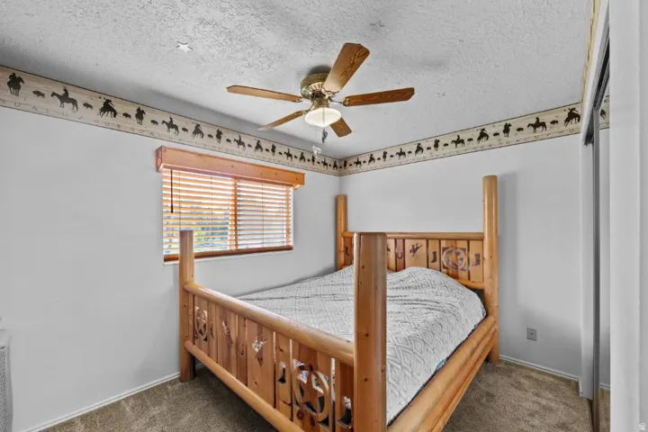 Master bedroom featuring a custom wooden four-poster bed with carved detailing, ceiling fan with wood blades, wood-framed window with horizontal blinds, and decorative border trim along the ceiling line