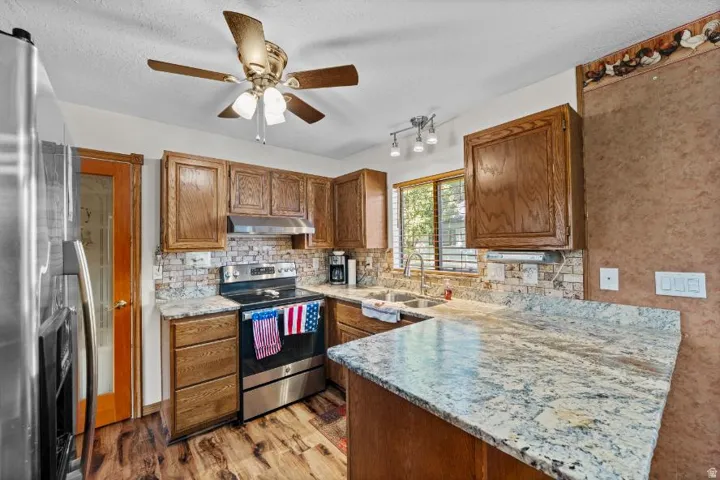 Kitchen featuring wood-finish flooring, wood cabinetry, stone countertops, and a tiled backsplash