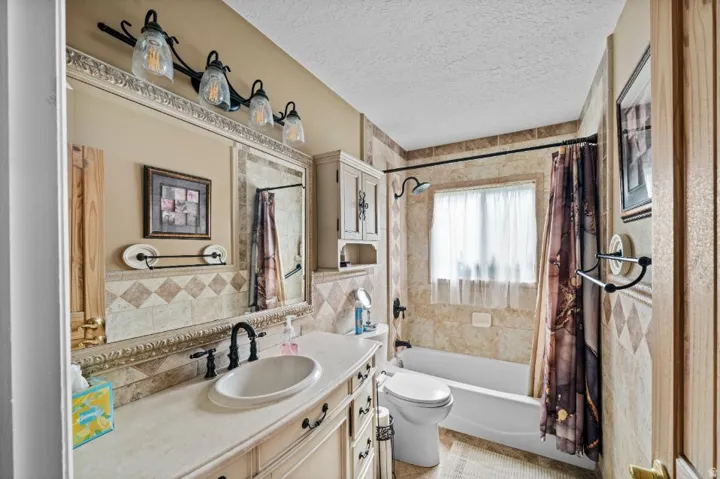 Spa-inspired bathroom featuring a ceramic pedestal sink with oil-rubbed bronze fixtures, ceramic tile backsplash with decorative border detailing, and a combined shower-tub enclosure with tile surround and coordinating curtain rod