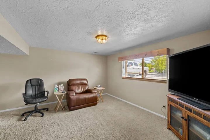 Versatile bonus room featuring neutral carpet flooring, a textured ceiling with recessed lighting, large windows with natural light, and a built-in entertainment center with wood cabinetry and media display