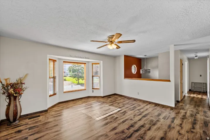 Wood-finish flooring, bay window with wood blinds, ceiling fan, and a partial wall with a decorative cutout